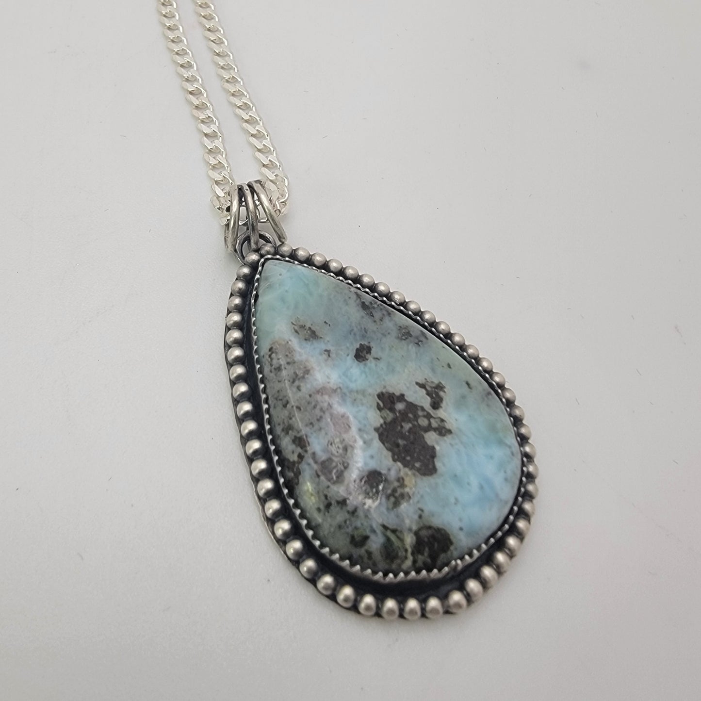 Blue teardop shaped gemstone bezel set pendant on white background