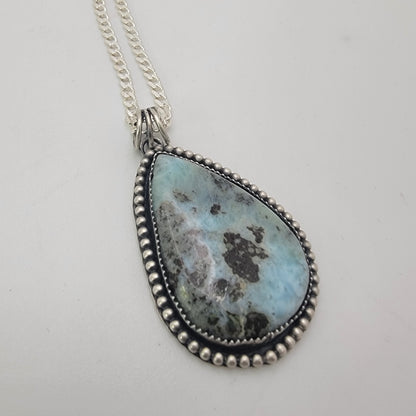 Blue teardop shaped gemstone bezel set pendant on white background