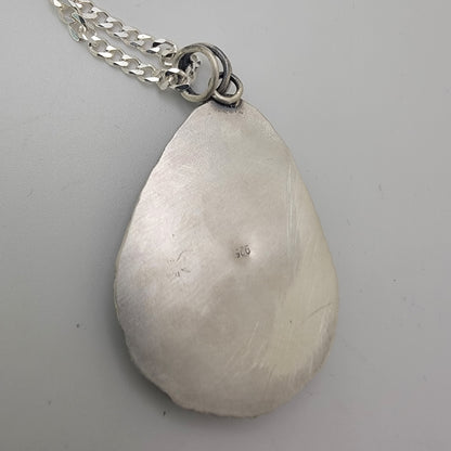 Back of silver teardrop shaped pendant on silver curb chain