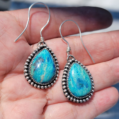 Pair of blue gemstone earrings bezel set in silver with oxidized beaded accent on silver hooks being held in a hand