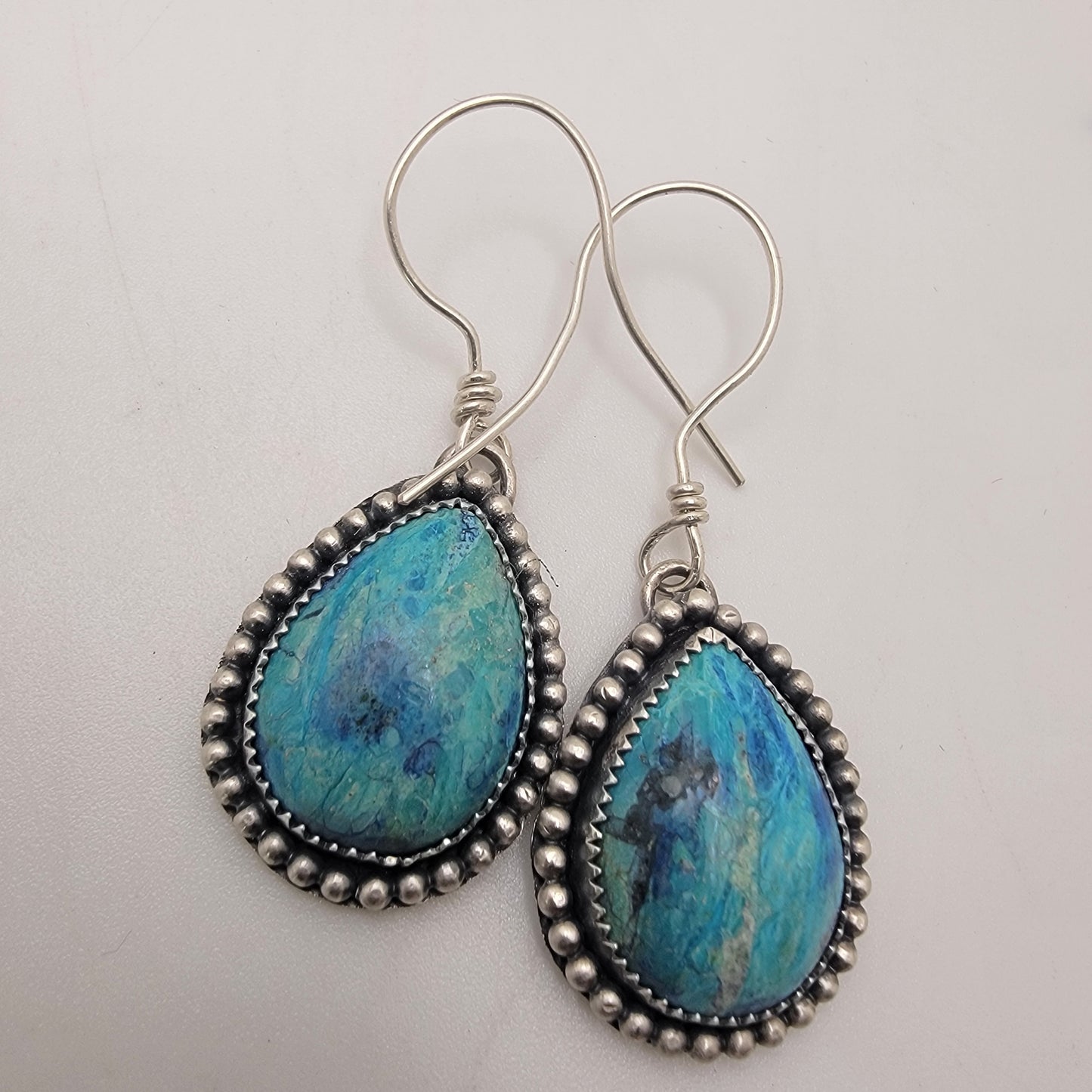 Pair of blue gemstone earrings bezel set in silver with oxidized beaded accent on silver hooks on a white background