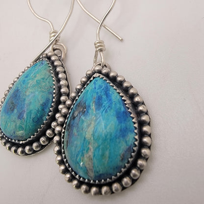 Pair of blue gemstone earrings bezel set in silver with oxidized beaded accent on silver hooks on a white background
