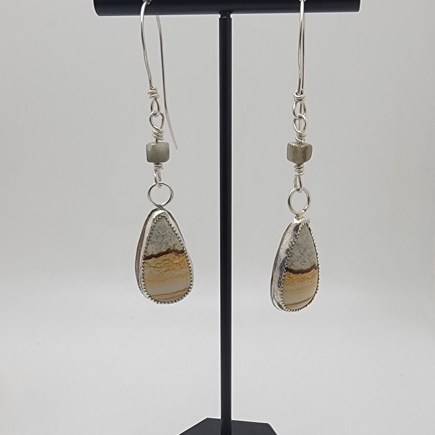 Pair of petrified wood teardrop shaped sterling silver earrings on black earrings stand against white background