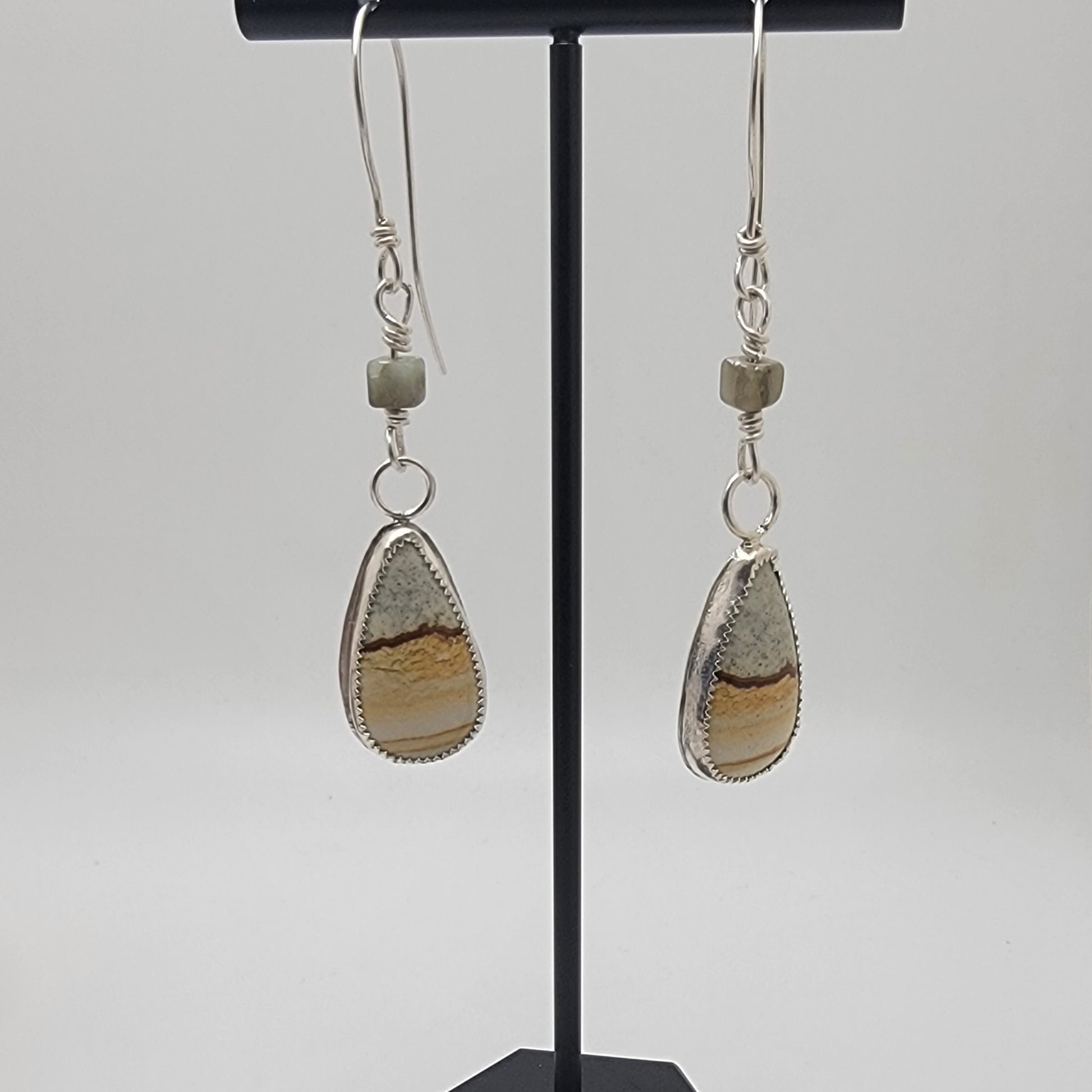 Pair of petrified wood teardrop shaped sterling silver earrings on black earrings stand against white background