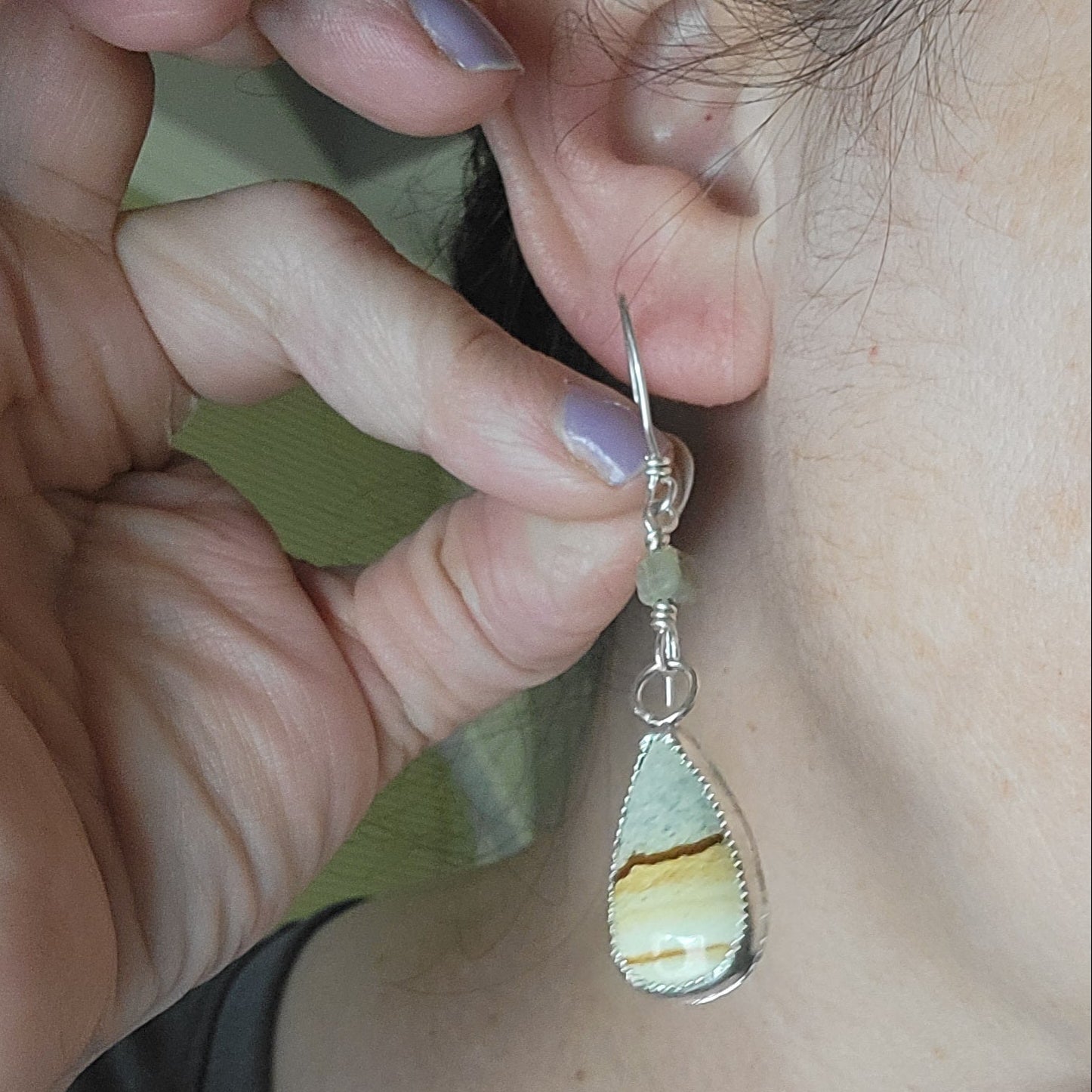 Petrified wood and sterling silver teardrop shaped dangle earrings being shown next to ear for scale