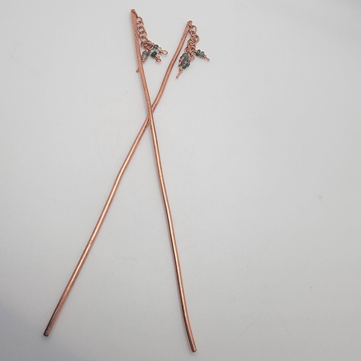 A pair of copper beaded hair sticks on a white background