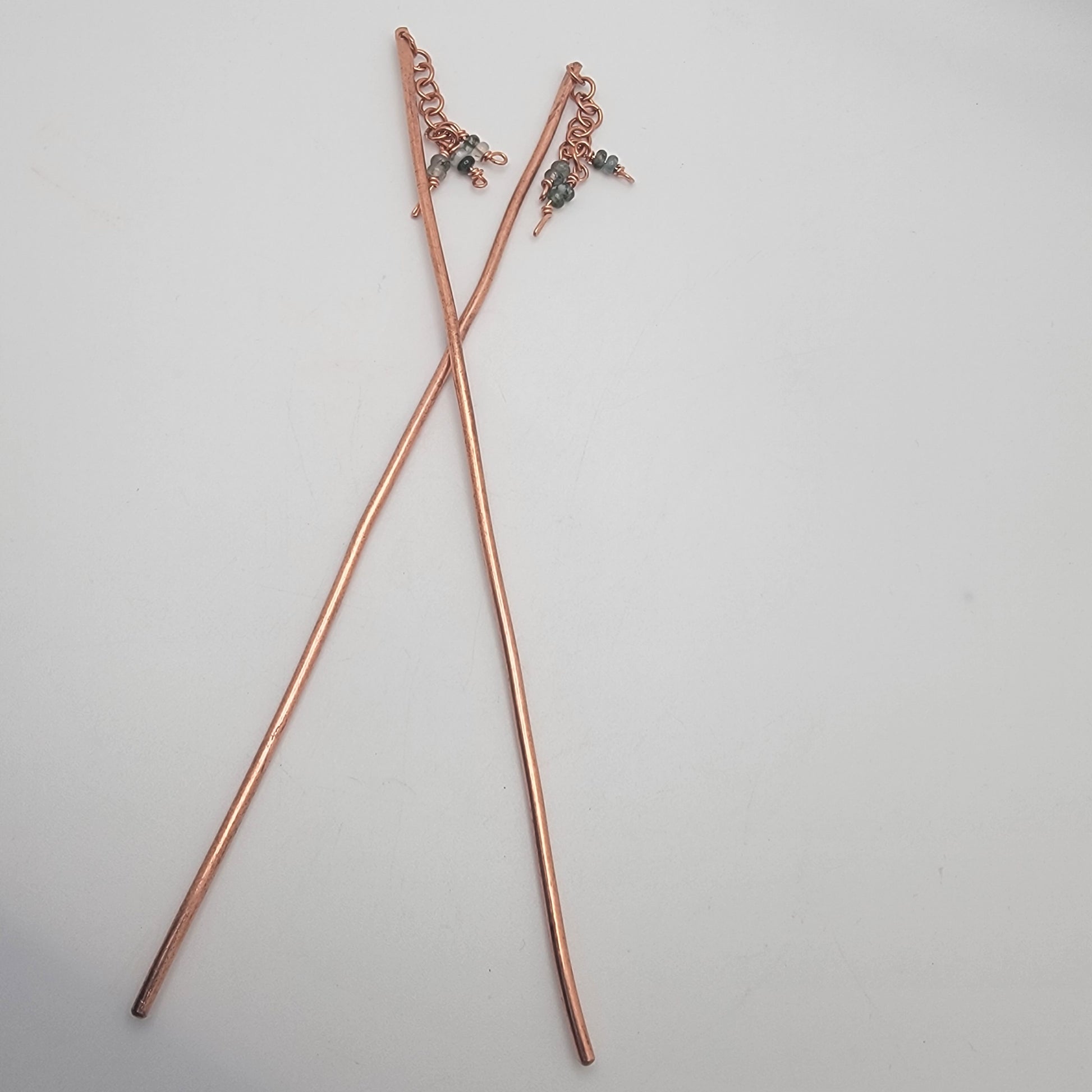 A pair of copper beaded hair sticks on a white background