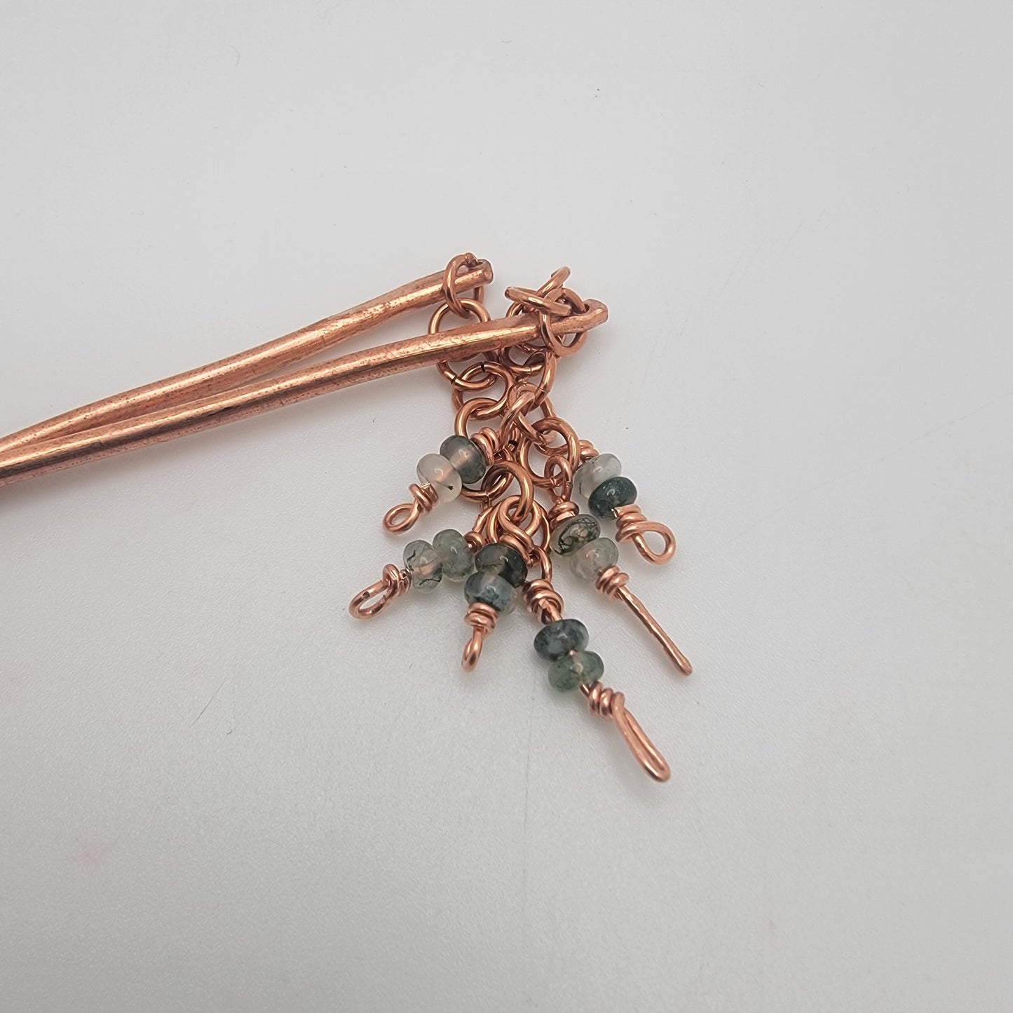 A closeup of the top of copper beaded hair sticks on a white background
