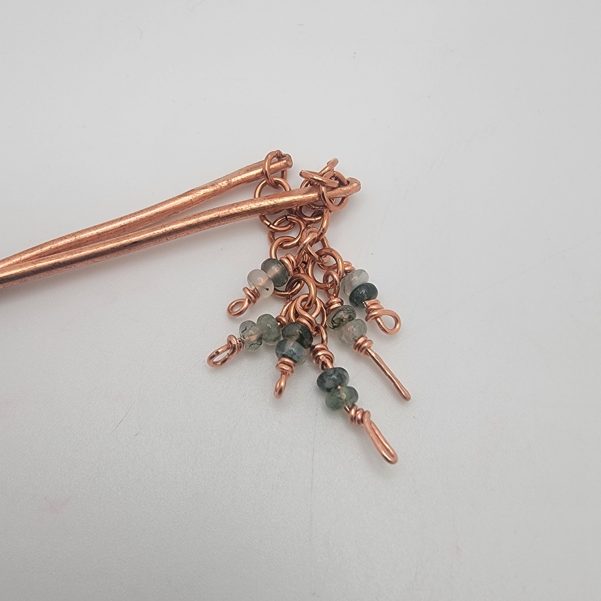 A closeup of the top of copper beaded hair sticks on a white background