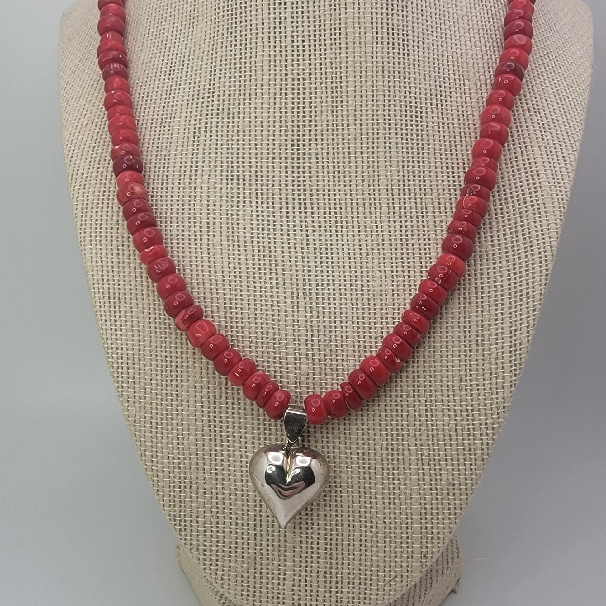 Red beaded neckalce with silver heart on beige necklace display against white background