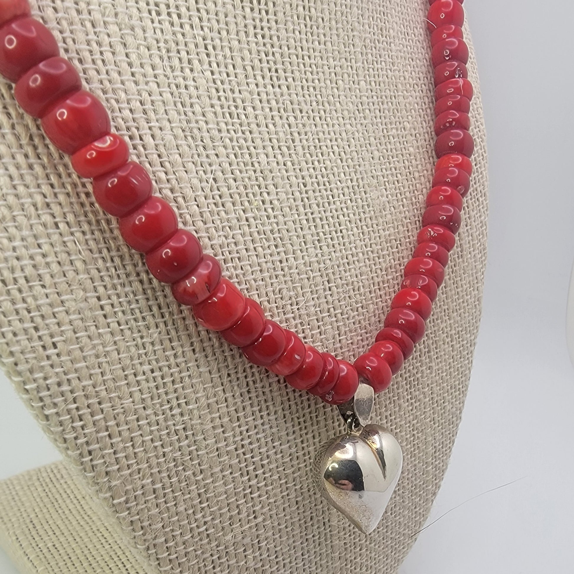 Red beaded neckalce with silver heart on beige necklace display against white background