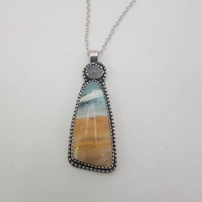 A silver pendant necklace featuring a teardrop-shaped stone with a marbled pattern of blue, white, and golden-brown, suspended from a silver chain against a plain white background.