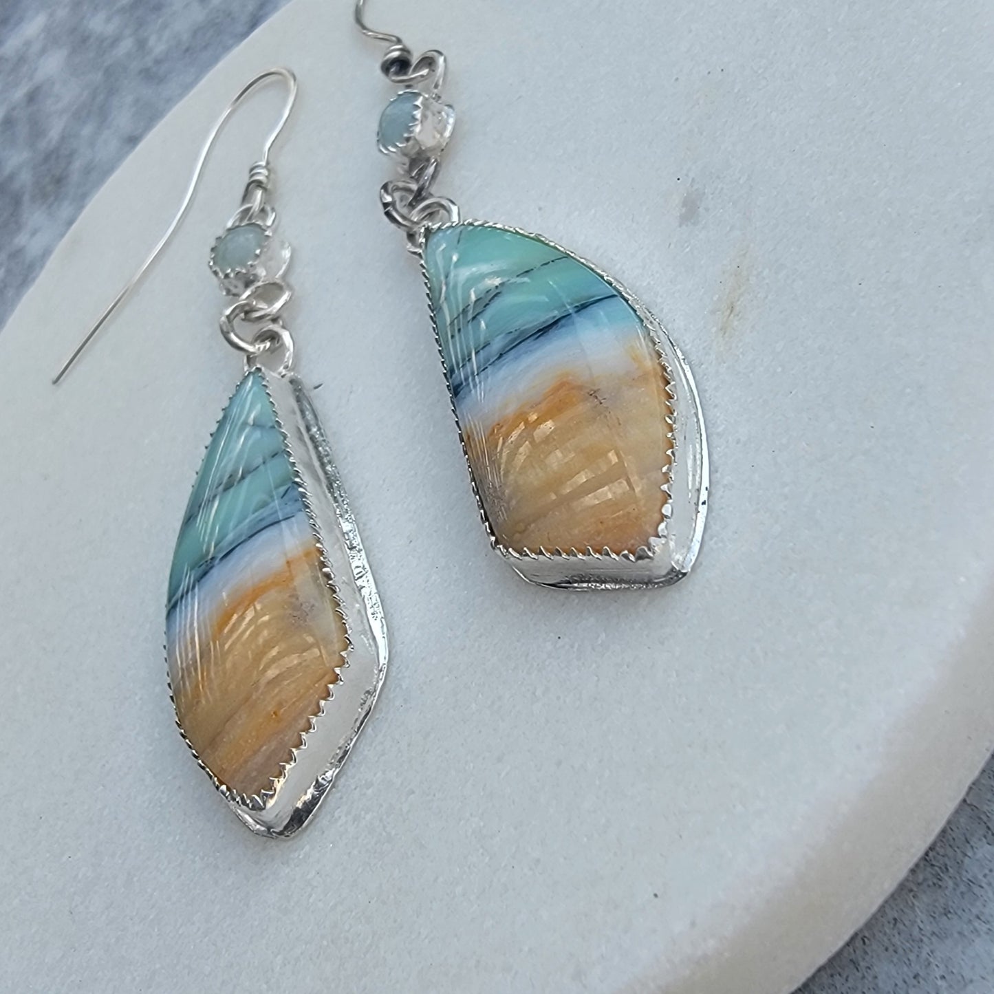 A pair of silver dangle earrings with marquise-shaped turquoise and amber stone inlays, displayed on a light gray surface.