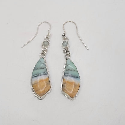 A pair of silver dangle earrings featuring marquise-shaped resin pendants with a marbled pattern of light blue, gray, and warm tan, hanging from silver fishhook wires on a plain light background.