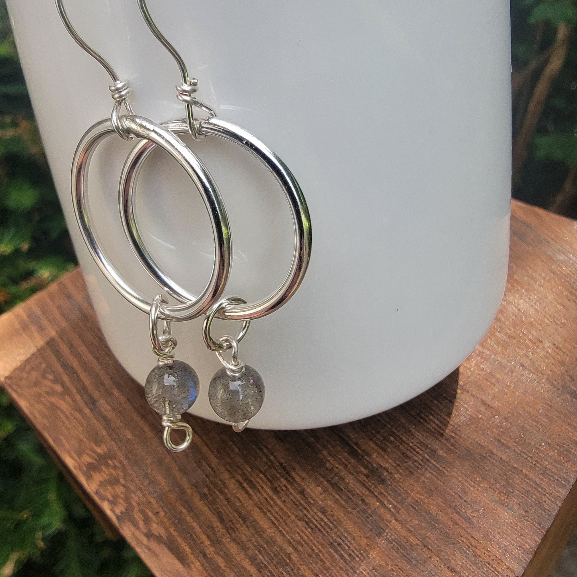 Silver hoop earrings with small gray stone bead drops, displayed on a white ceramic vase resting on a wooden surface.