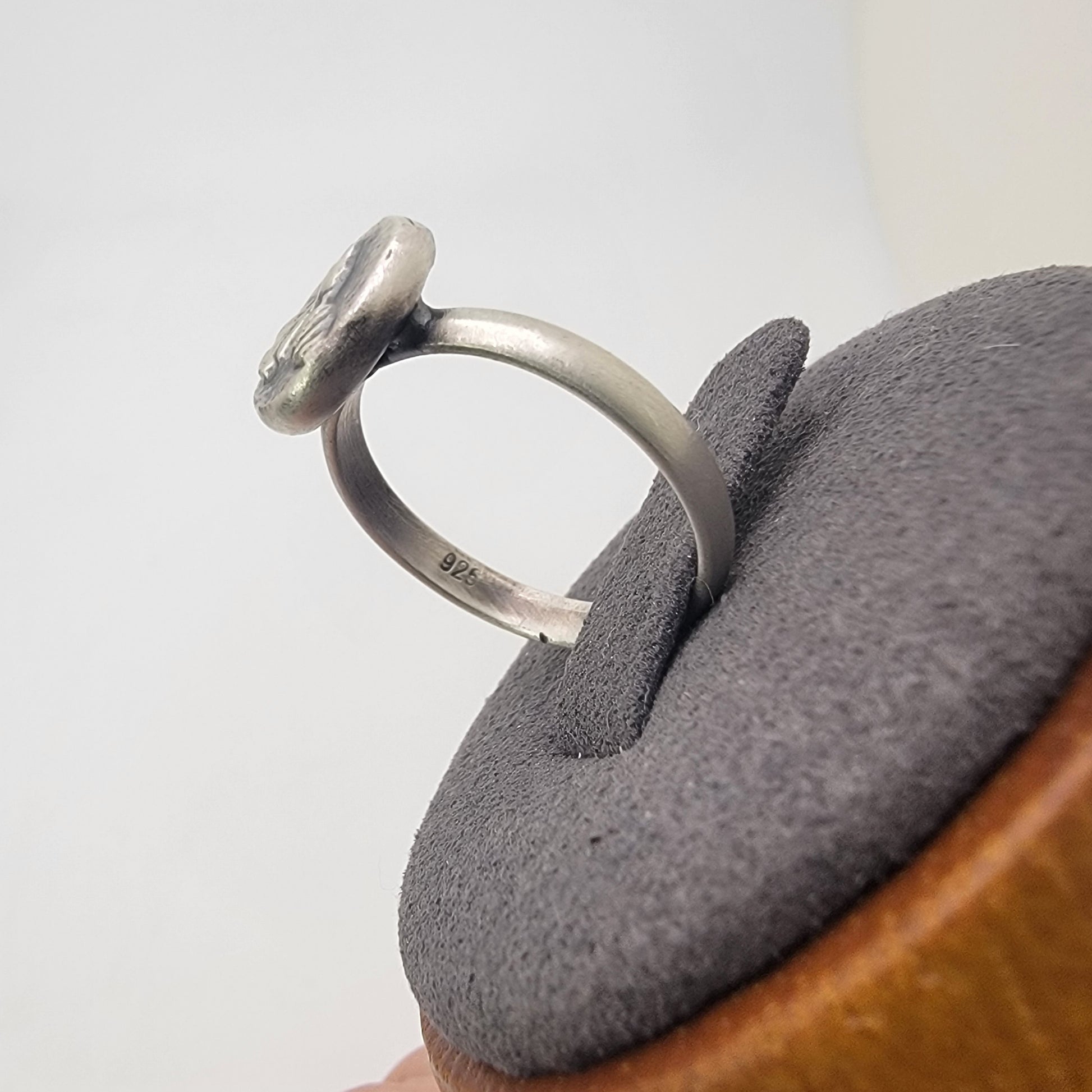 A sterling silver ring with a flat, circular disc-like top, displayed on a gray velvet ring stand.
