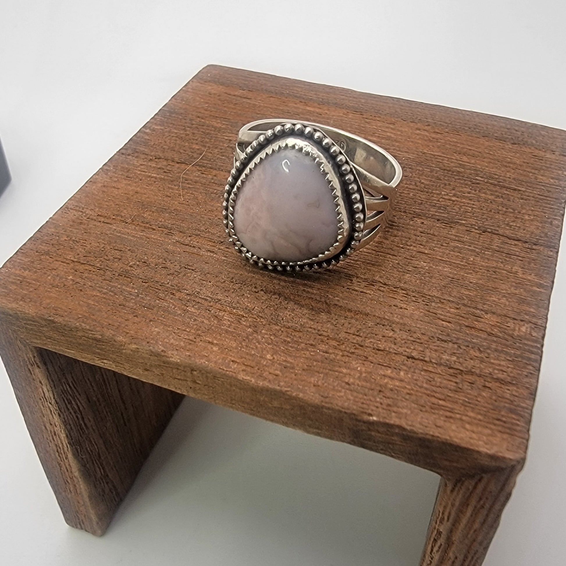 Pink gemstone and sterling silver ring with oxidized beaded detail on a wood platform