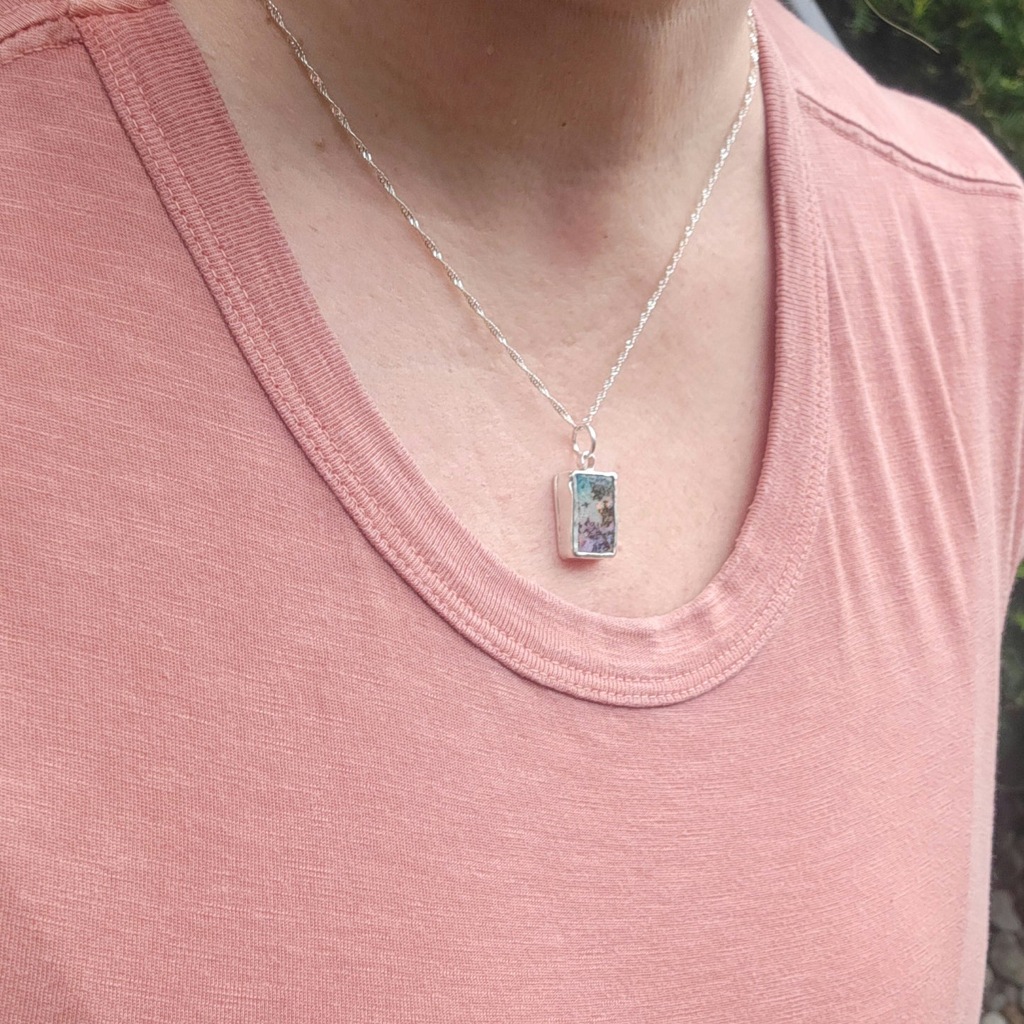 A close-up of a person wearing a silver chain necklace with a small rectangular boulder opal and sterling silver pendant 
