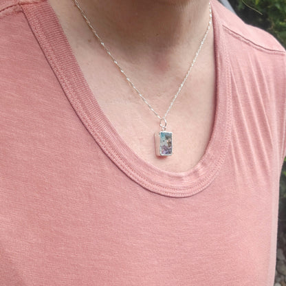 A close-up of a person wearing a silver chain necklace with a small rectangular boulder opal and sterling silver pendant 