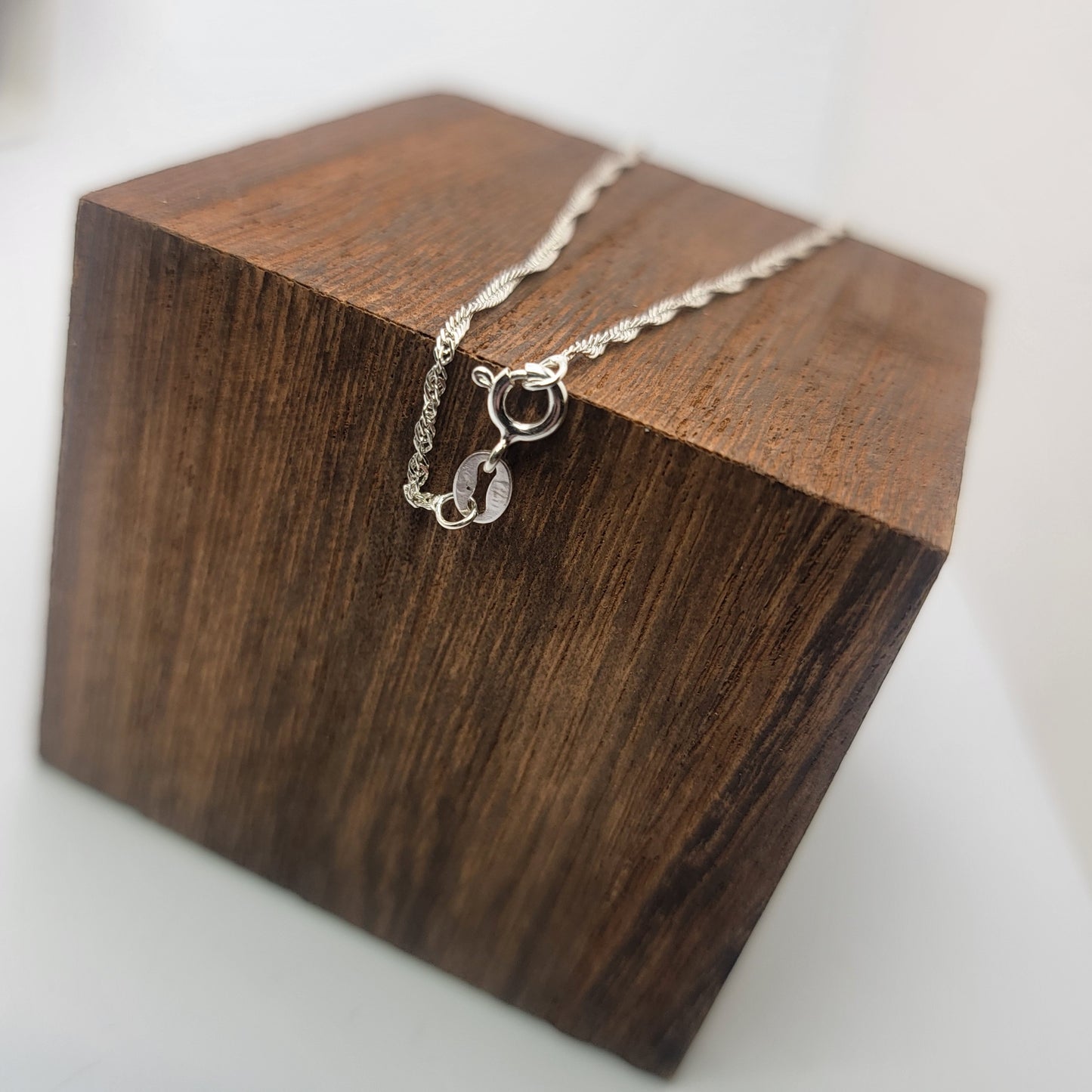A silver chain necklace with a spring clasp and stamped 925, displayed on a dark brown wooden block against a white background.