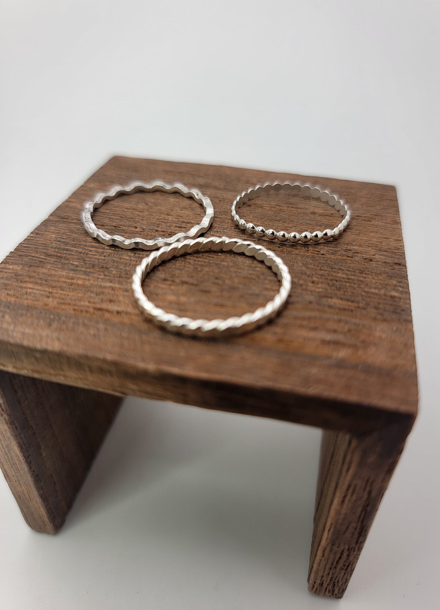 Three textured silver rings displayed on a small wooden stand against a light gray background.