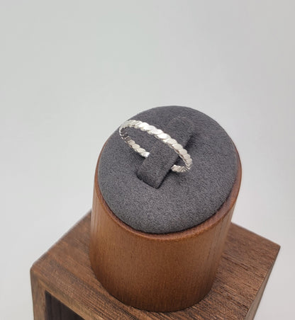 A silver twisted rope ring displayed on a gray velvet ring stand, which sits on a wooden block against a light gray background.