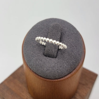 A delicate silver beaded ring displayed on a gray velvet ring stand, which sits on a wooden cube against a light gray background.