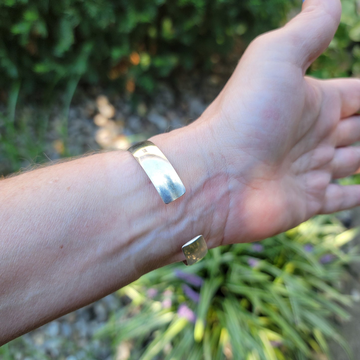 Back view od silver bangle bracelet with open back worn on wrist next to natural outdoor environment