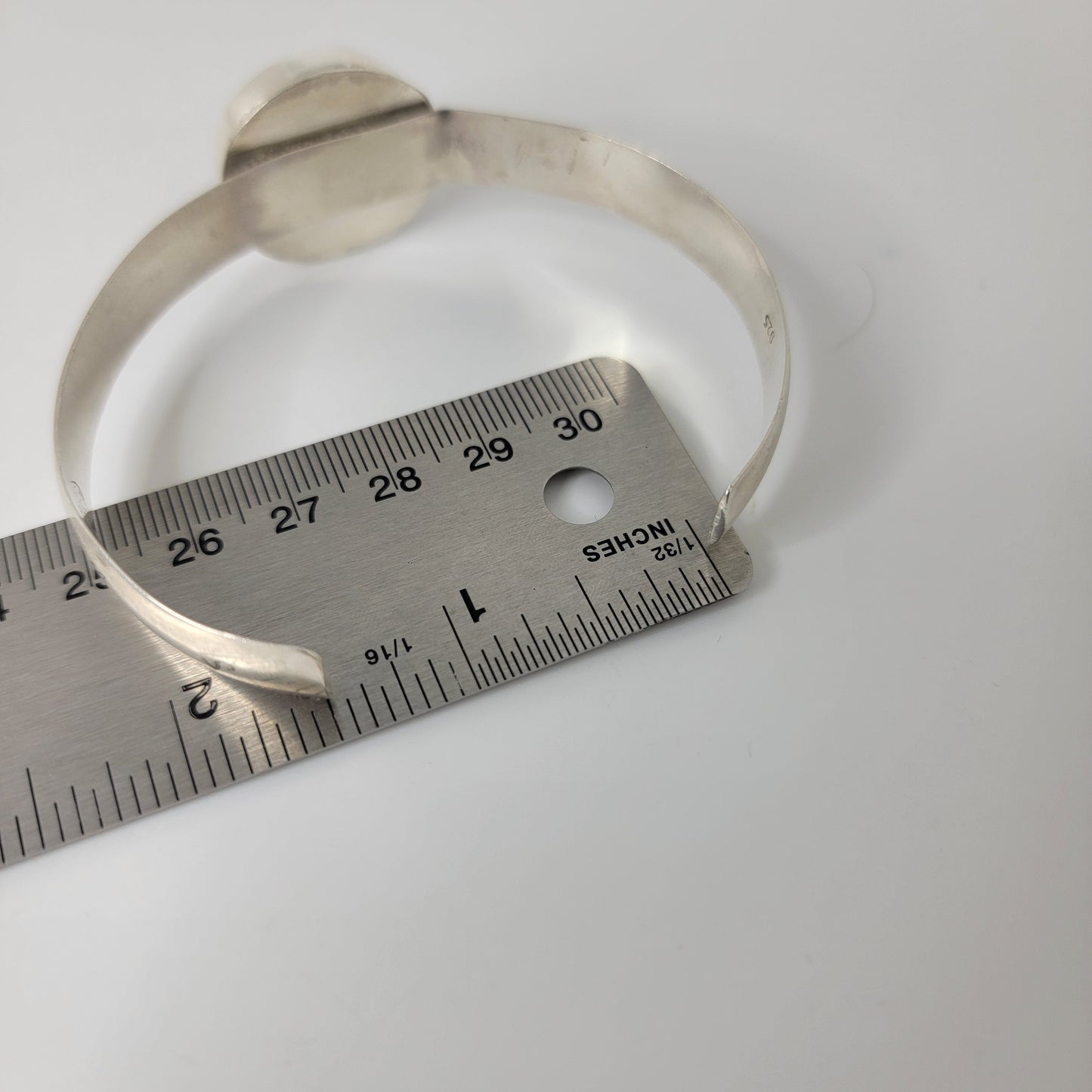 Silver bangle bracelet next to ruler for scale on white background