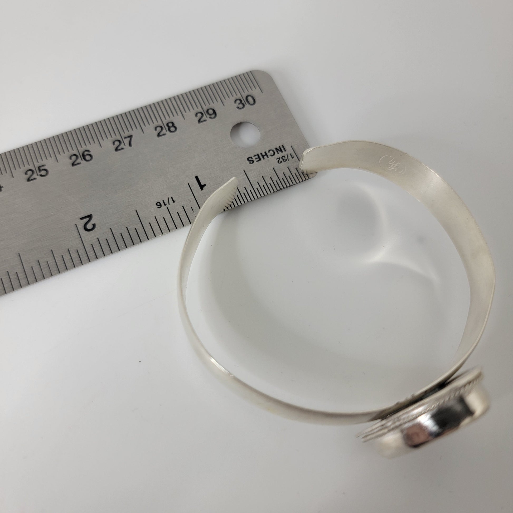 A silver cuff bracelet with bezel set cabochon shown on a white background, with a metal ruler placed beside it for scale.