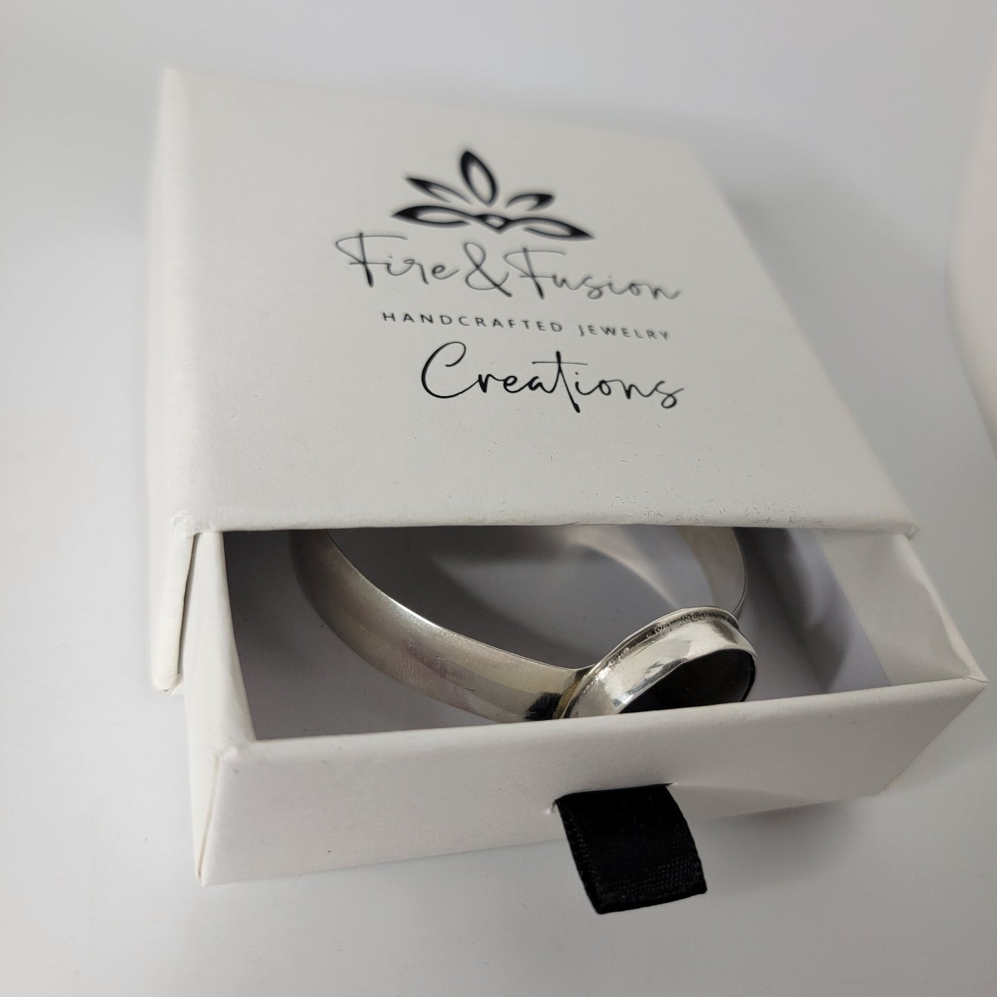 A silver bracelet displayed inside an open white jewelry box with the brand name 'Fire & Fusion Creations' printed on the lid, set against a clean white background.