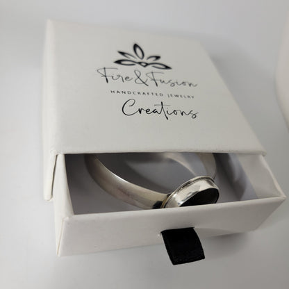 A silver bracelet displayed inside an open white jewelry box with the brand name 'Fire & Fusion Creations' printed on the lid, set against a clean white background.