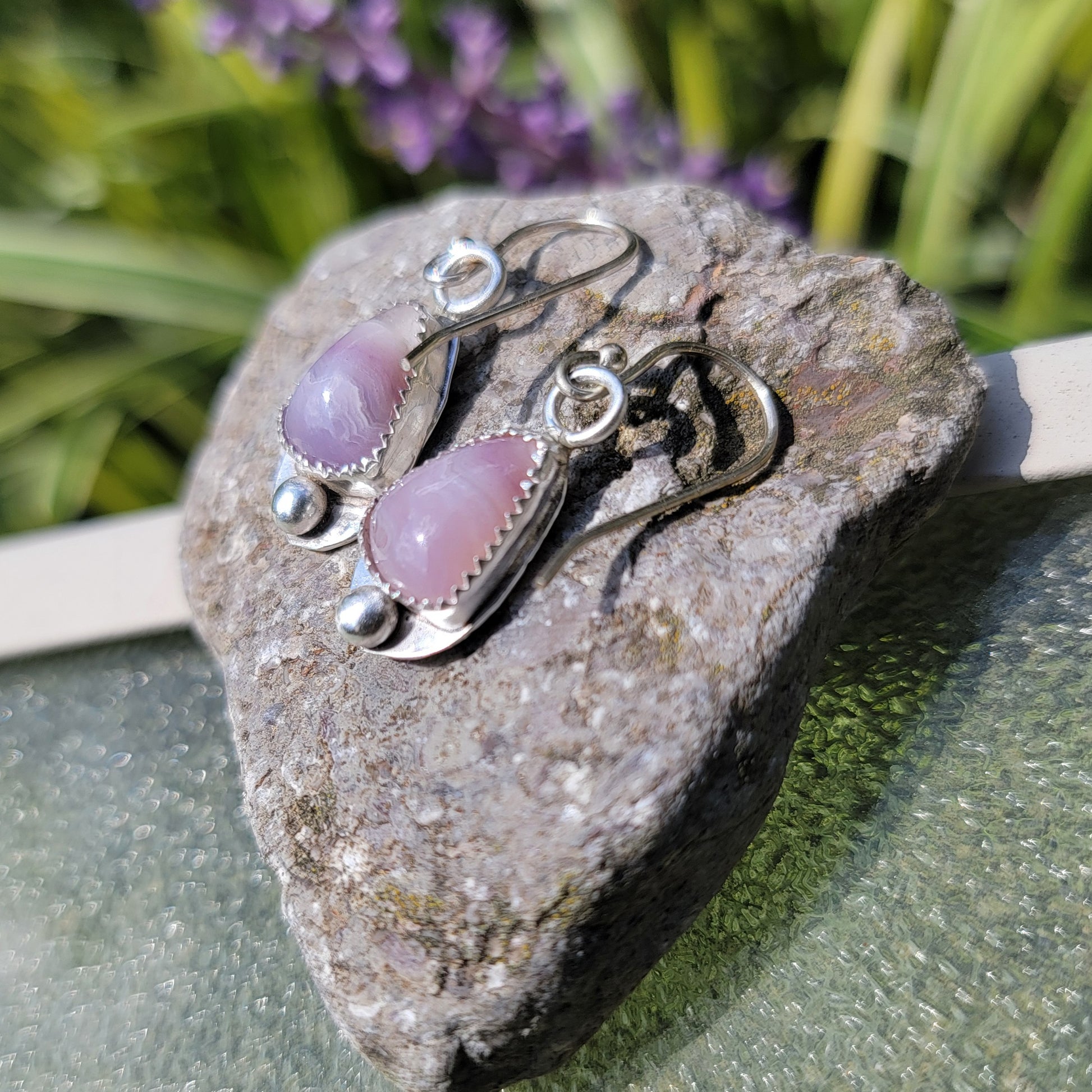 A pair of kunzite and sterling silver earrings displayed on a rock next to a natural outdoor environment