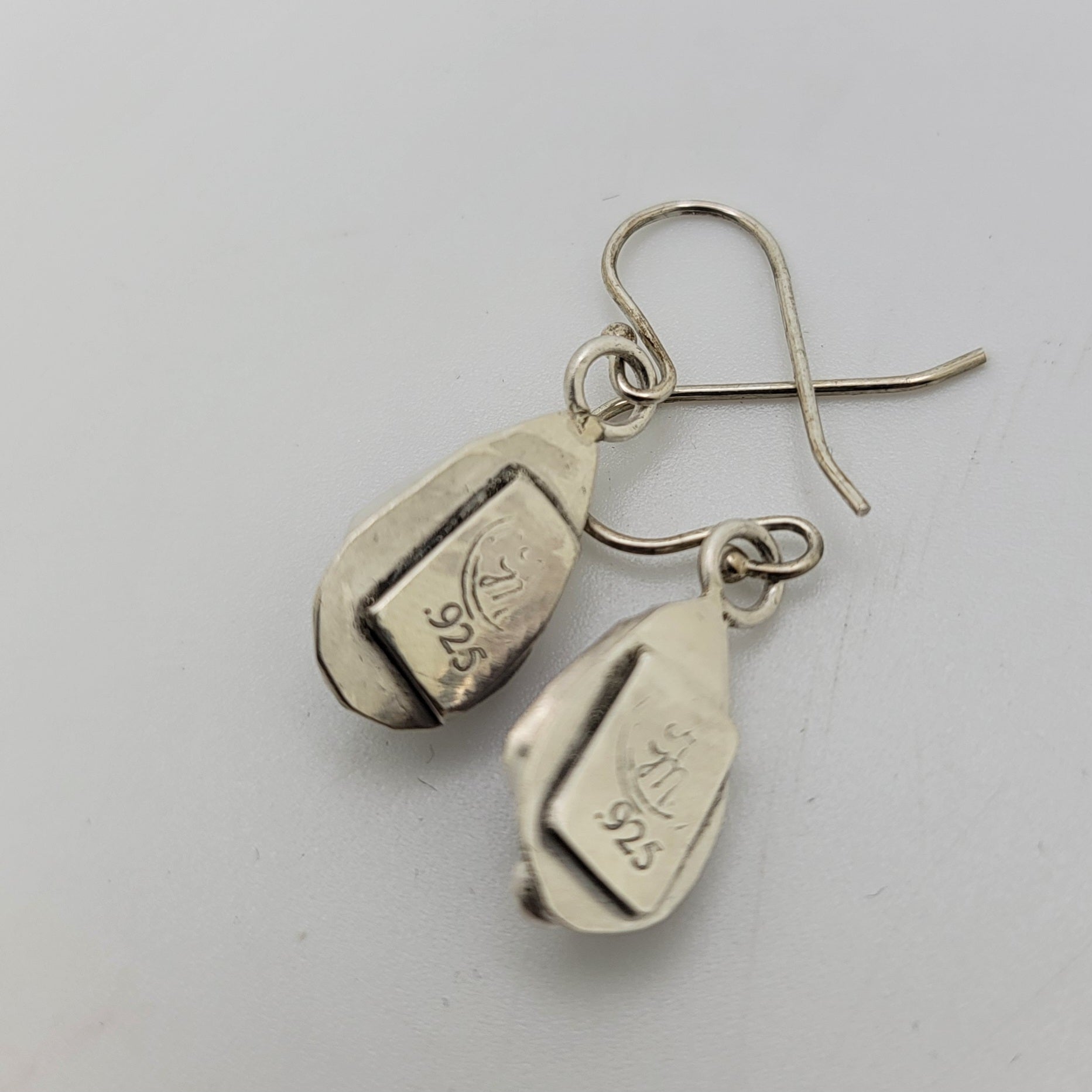 A pair of sterling silver dangle earrings with fishhook wires, featuring engraved 925 silver purity stamps on the teardrop-shaped pendants, shown on a light gray background.