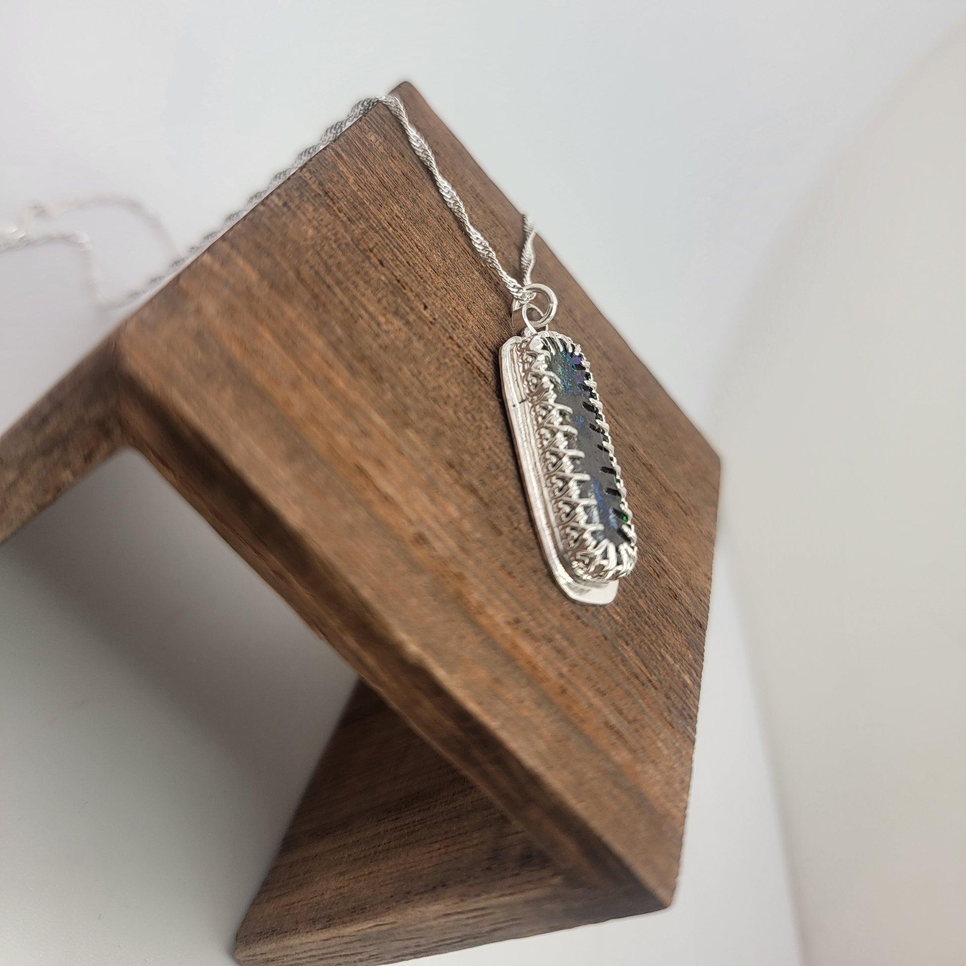 A silver rectangular pendant necklace with a dark blue inlay, displayed on a wooden stand against a white background.