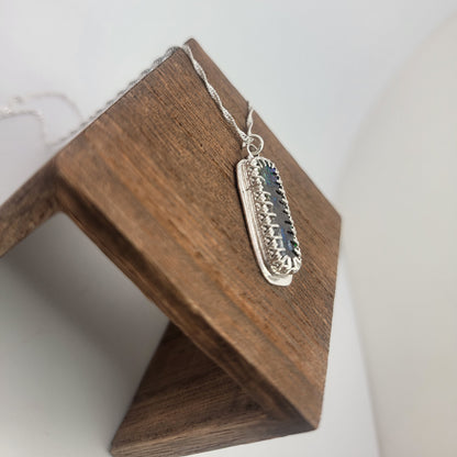 A silver rectangular pendant necklace with a dark blue inlay, displayed on a wooden stand against a white background.