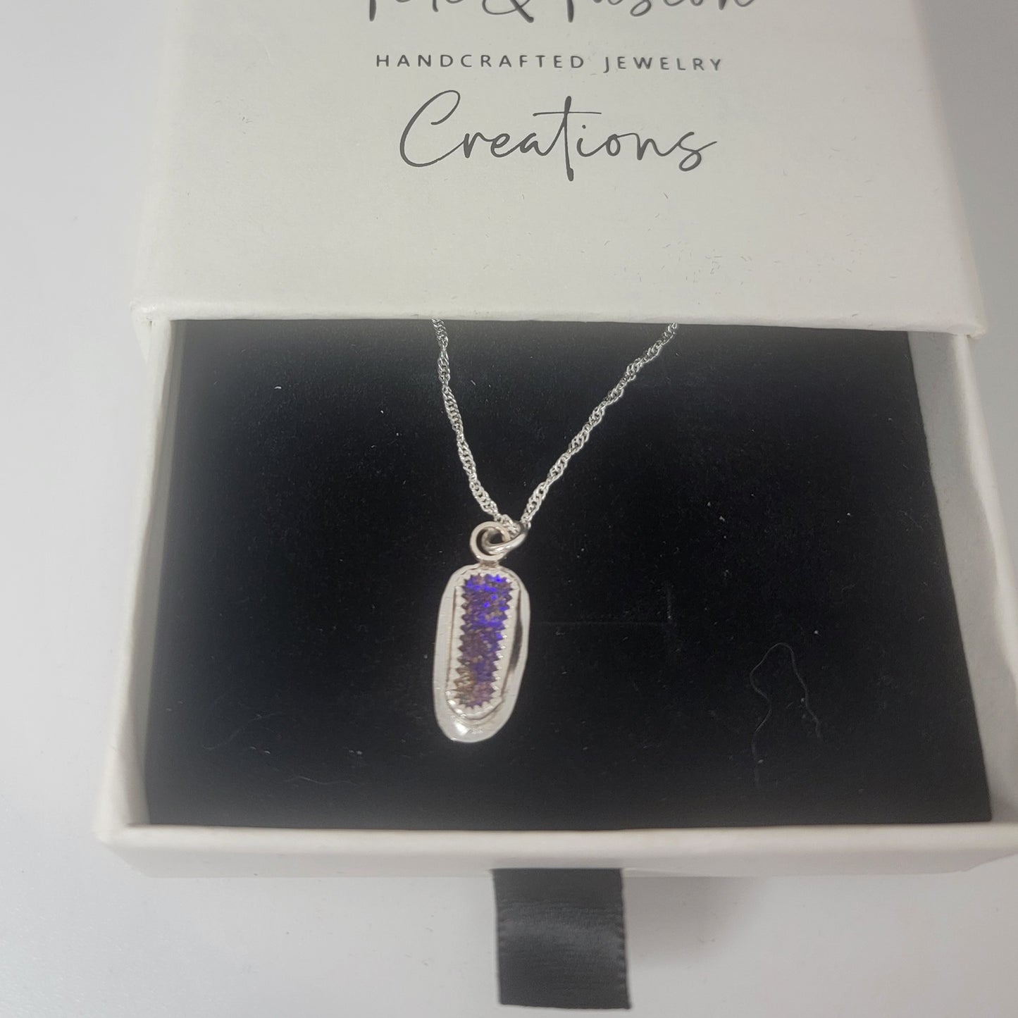 A silver pendant necklace with a purple textured inlay, displayed inside an open white jewelry box with a black velvet insert. The inside lid of the box is printed with the brand name 'Tinsley & Tinsley Creations'.