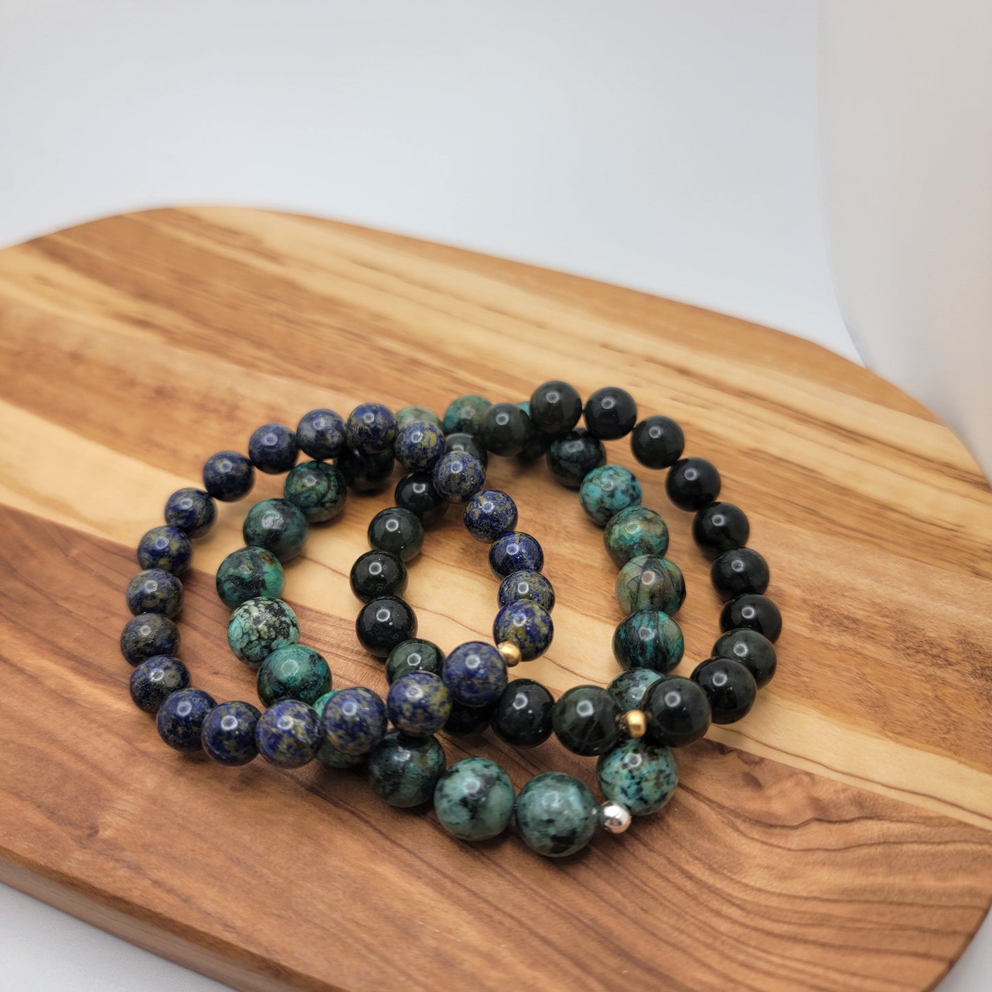 3 gemstone stretch bracelets in lapis, deep green jade and african turquoise on a wood surface on a white background