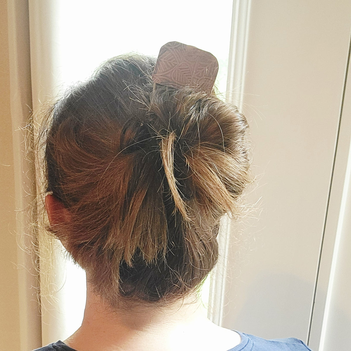Brass and Leaf Design Copper Hair Fork shown in a person's hair with updo next to a window