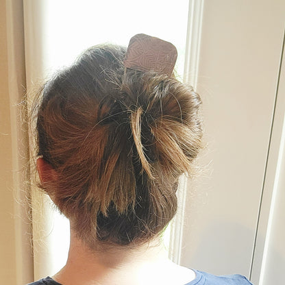 Brass and Leaf Design Copper Hair Fork shown in a person's hair with updo next to a window