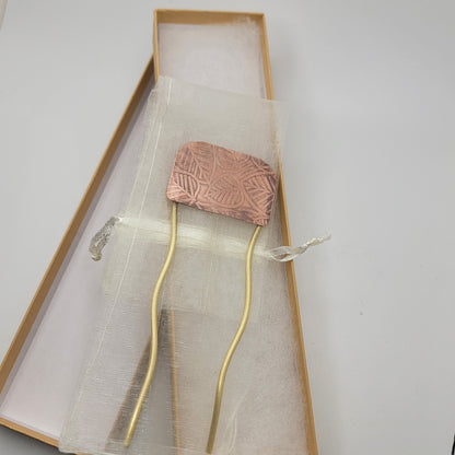 Brass and leaf patterned copper hair fork shown in organza pouch on top of gift box