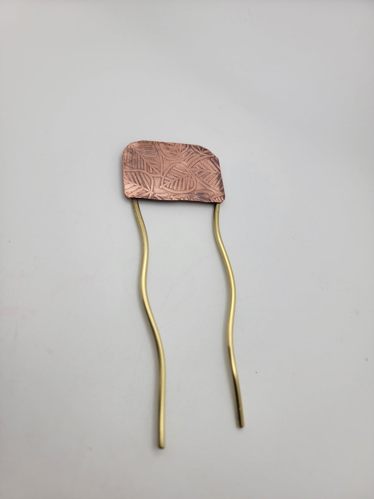 Brass and leaf patterned copper hair fork on white background