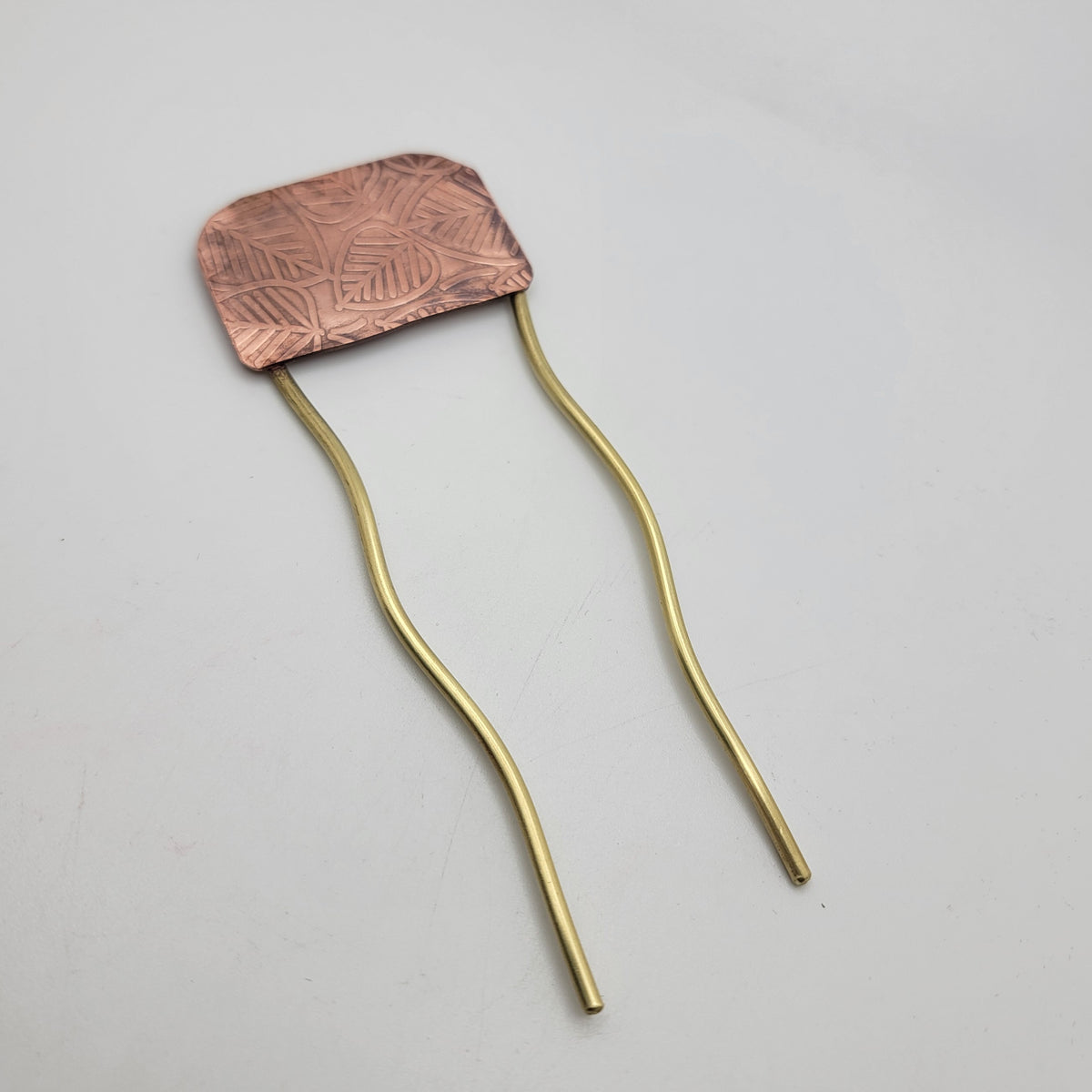 Brass and leaf patterned copper hair fork on white background