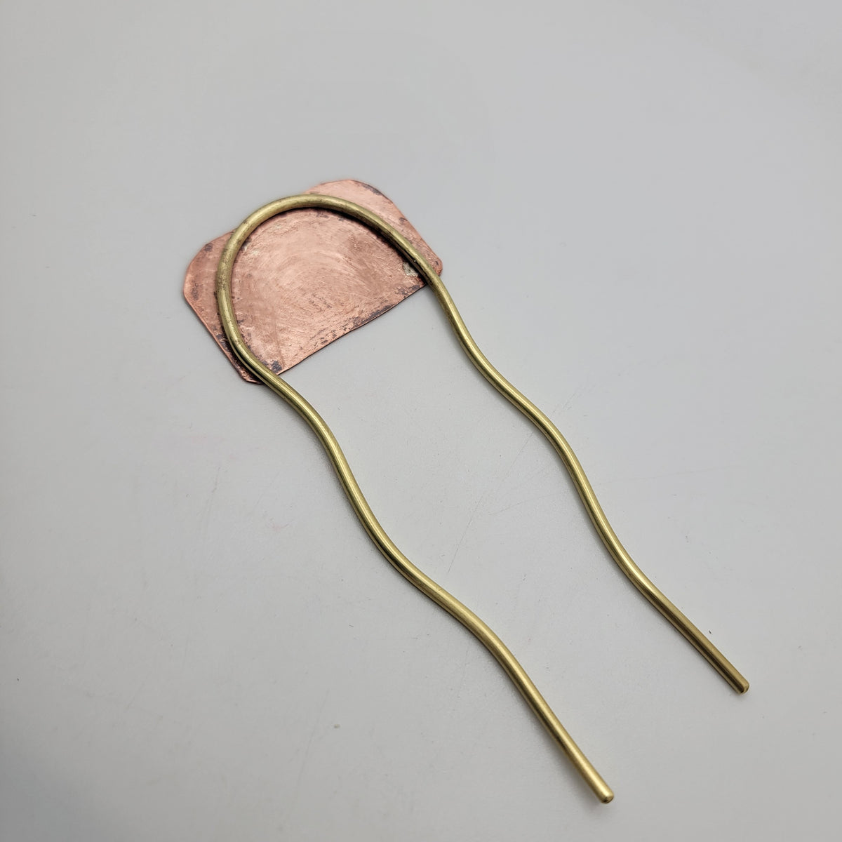 Back view of brass and leaf patterned copper hair fork on white background