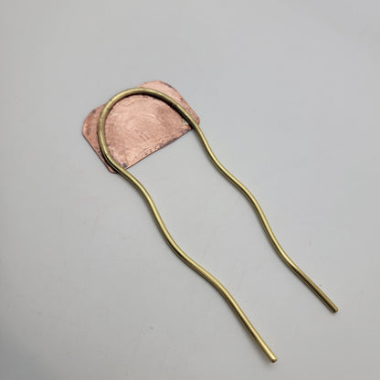 Back view of brass and leaf patterned copper hair fork on white background