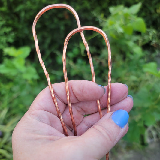 2 copper hair pins with twist design being held by a hand in natural outdoor environment