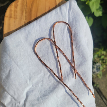 2 copper hair pins with twist design on white cloth on wood platform in natural outdoor environment
