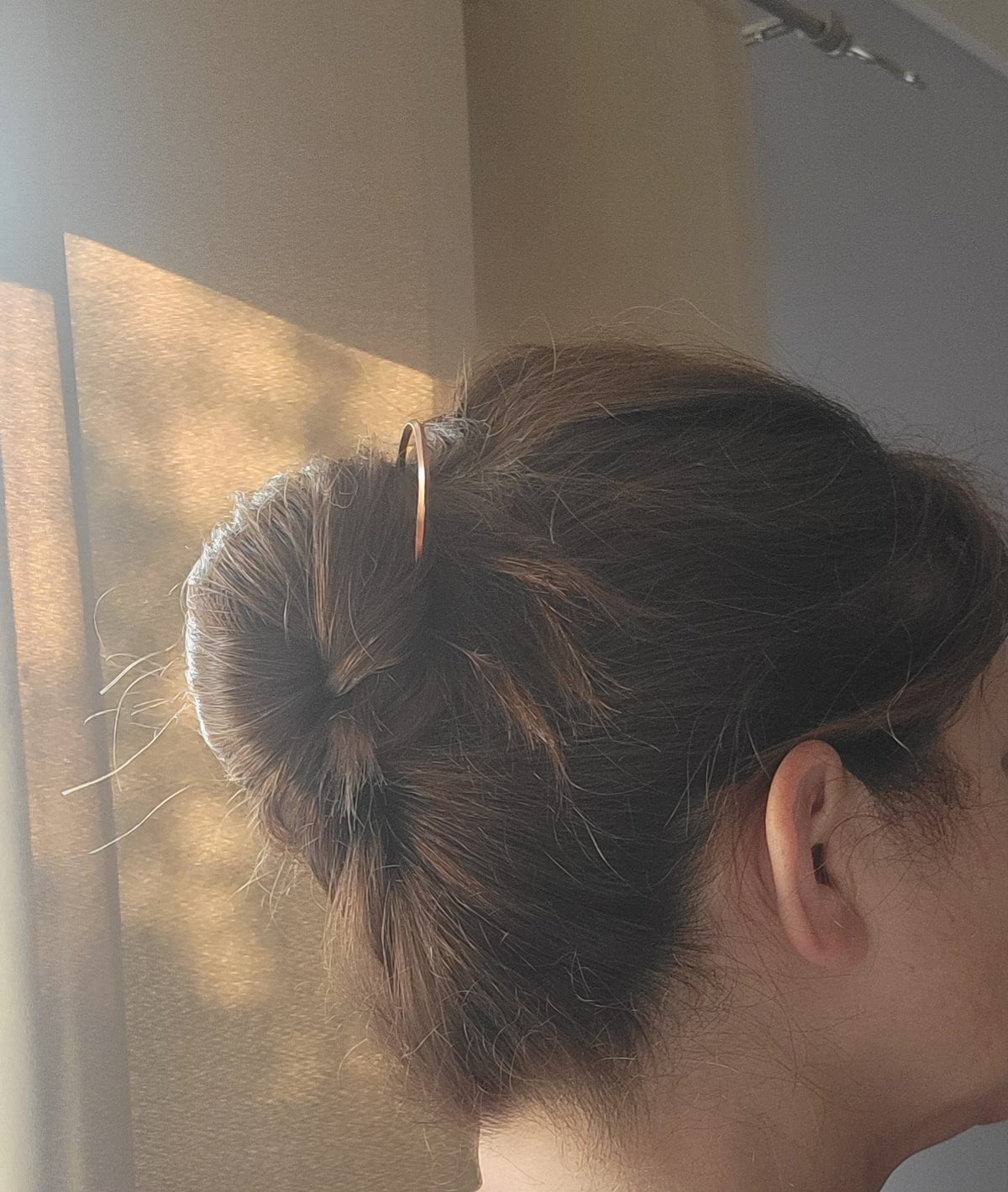 2 copper hair pins with twist design being worn in hair with updo next to a window with a beige curtain