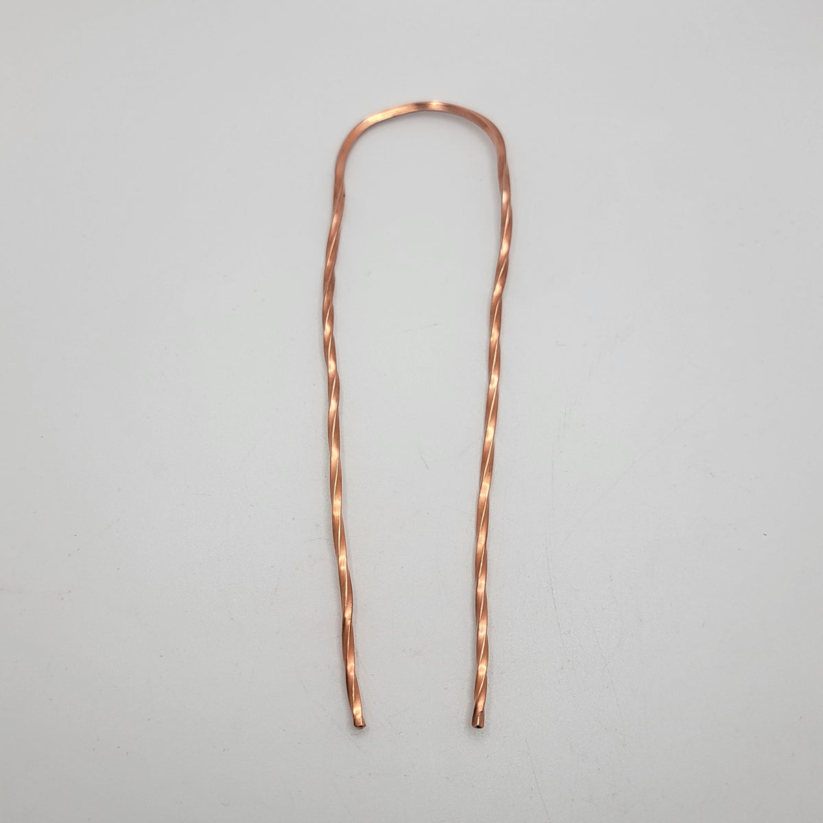 A single copper hair pin with twist design on a white background