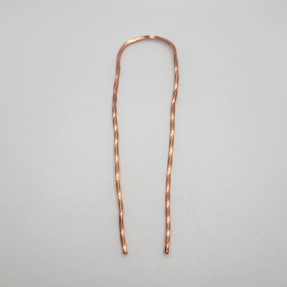 A single copper hair pin with twist design on a white background